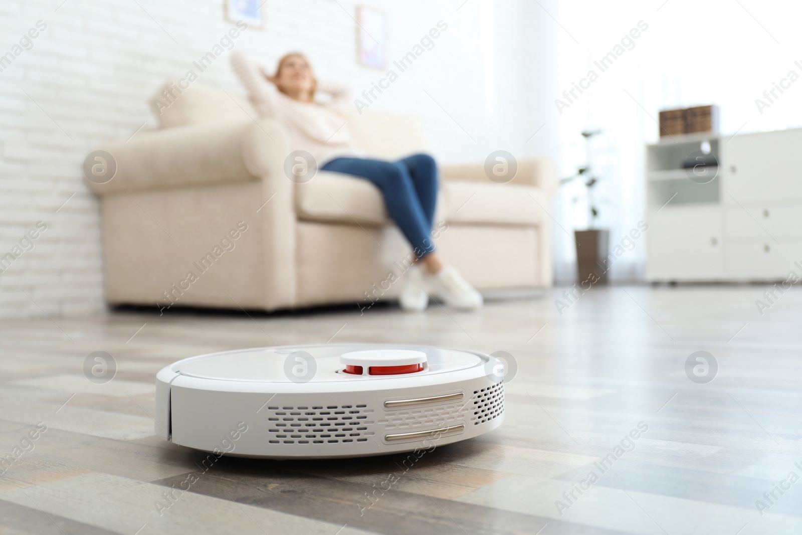 Photo of Woman resting while robotic vacuum cleaner doing her work at home