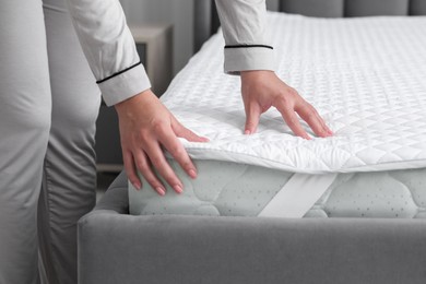 Photo of Woman touching new soft mattress on grey bed in bedroom, closeup