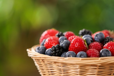 Photo of Wicker bowl with different fresh ripe berries outdoors, closeup. Space for text