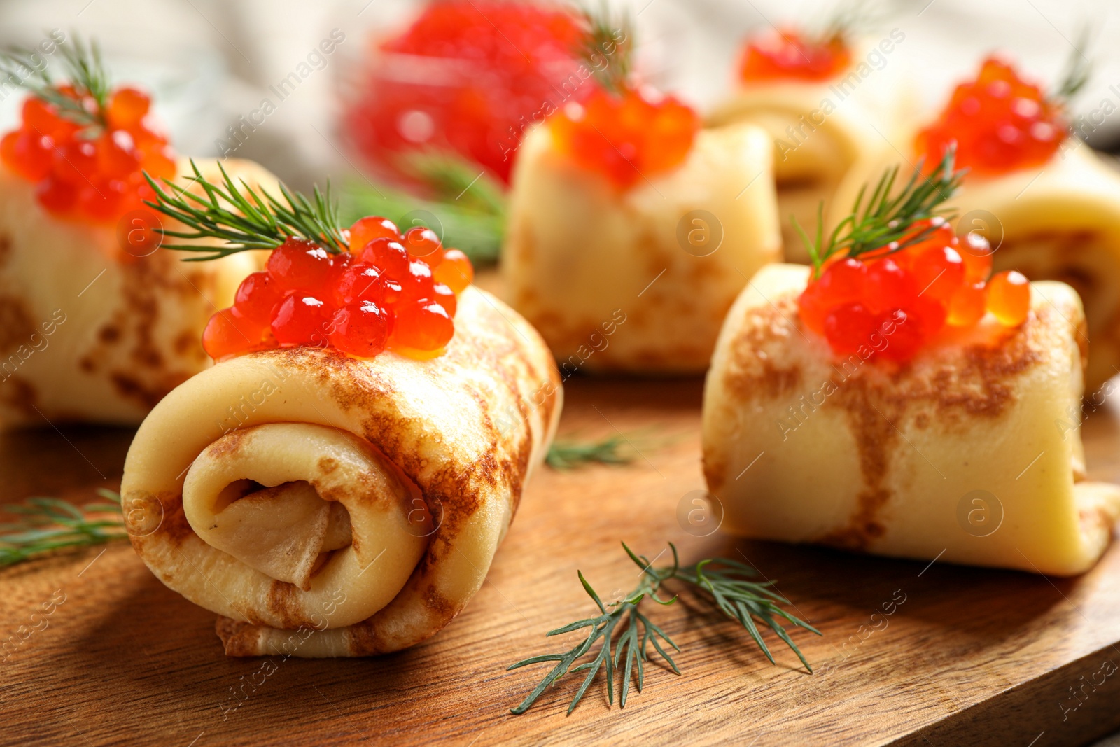 Photo of Delicious thin pancakes with red caviar on wooden board, closeup