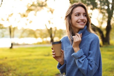 Photo of Beautiful young woman with coffee cup wearing stylish sweater in autumn park