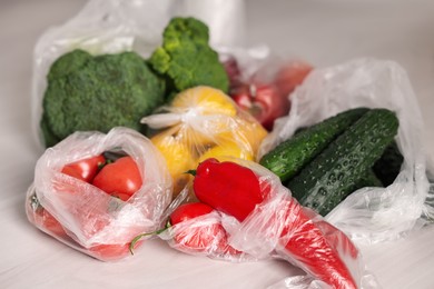 Photo of Plastic bags and fresh products on white table, closeup