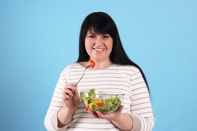 Photo of Beautiful overweight woman eating salad on light blue background. Healthy diet