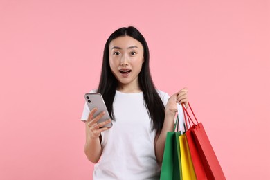 Surprised woman with shopping bags on pink background