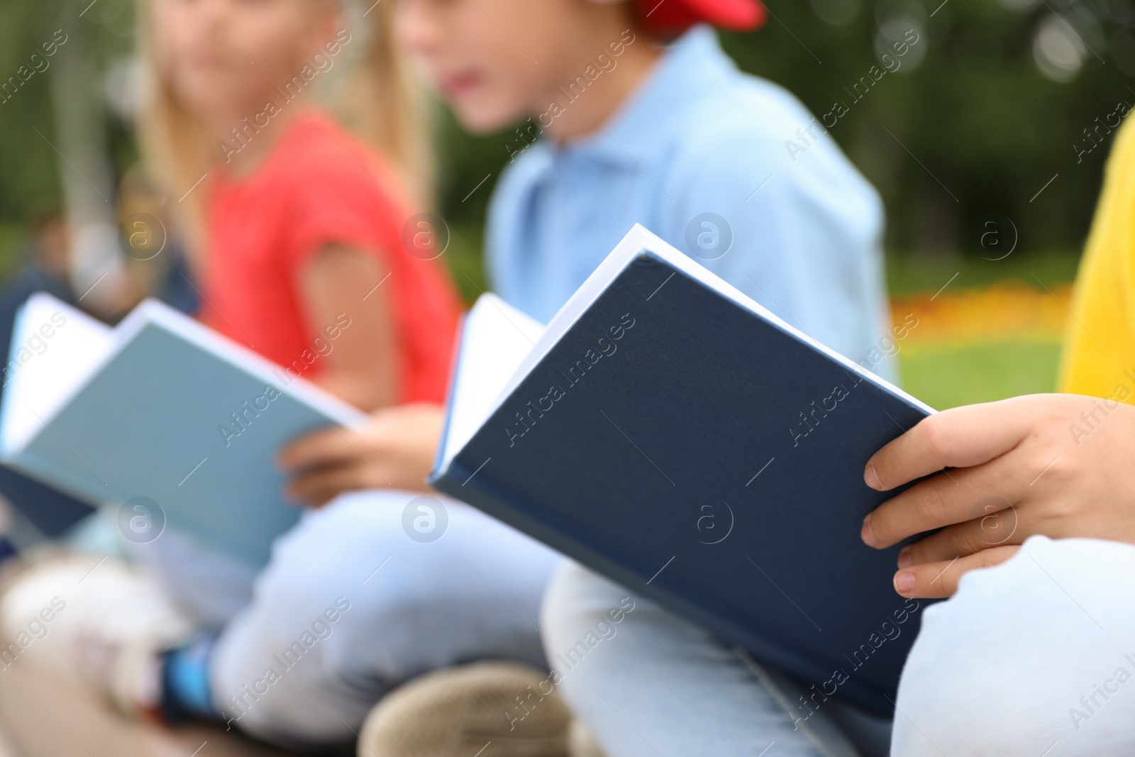 Photo of Little children reading books outdoors, closeup