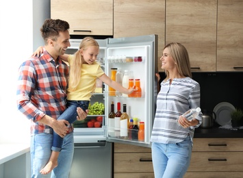 Photo of Happy family with bottle of water near refrigerator in kitchen