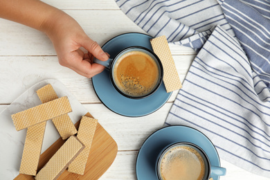 Woman having breakfast with delicious coffee and wafers at white wooden table, top view