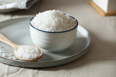 Photo of Organic salt in bowl and wooden spoon on table, closeup