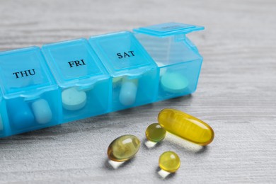 Photo of Weekly pill box with medicaments on wooden table, closeup