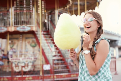 Photo of Young woman with cotton candy in amusement park. Space for text