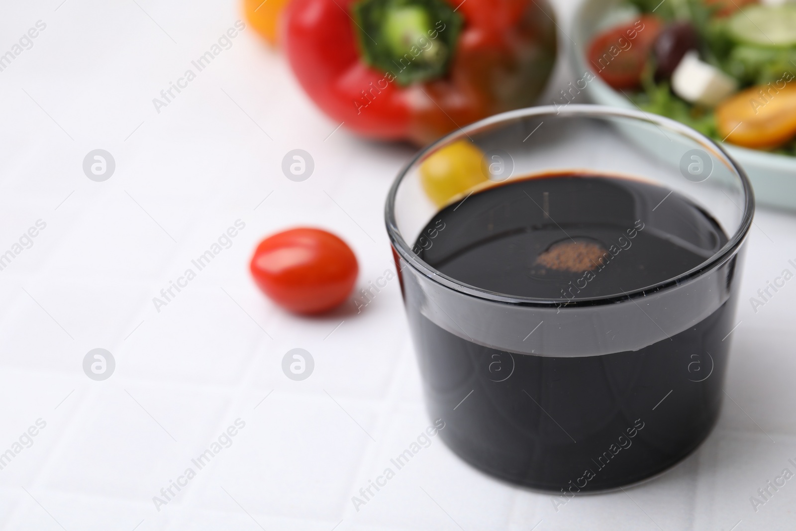 Photo of Vinegar in glass on white tiled table, closeup. Space for text