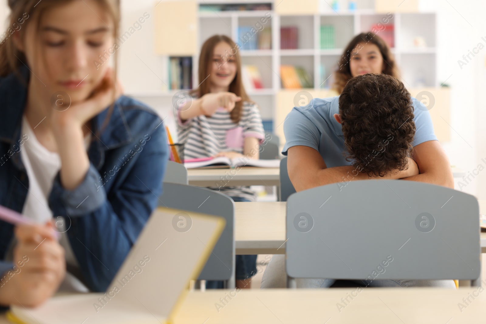 Photo of Teen problems. Lonely boy sitting separately from other students in classroom