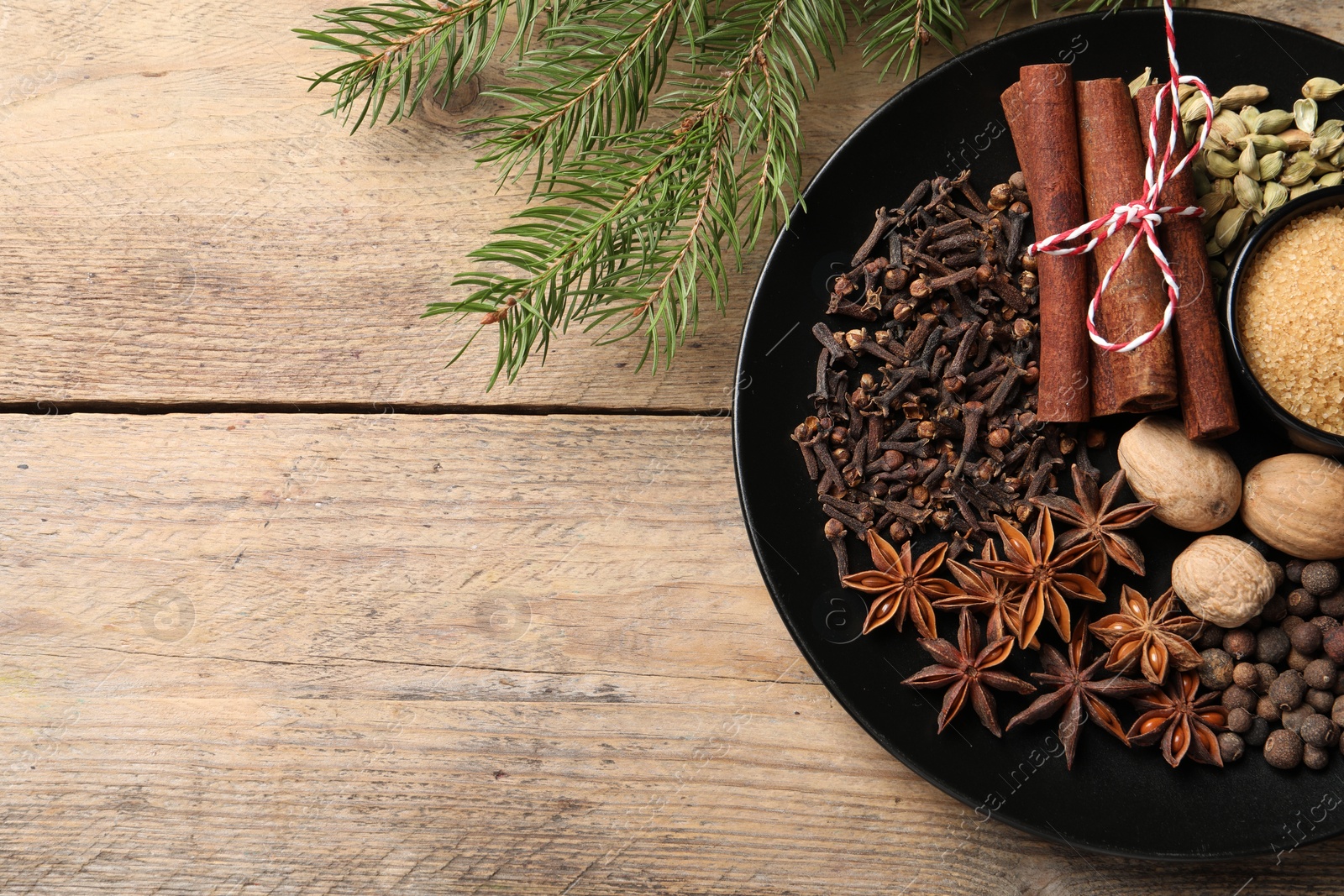 Photo of Dishware with different spices and fir branches on wooden table, flat lay. Space for text