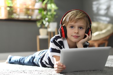 Photo of Cute little boy with headphones and tablet listening to audiobook at home