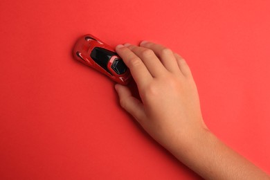 Photo of Child playing with toy car on red background, top view