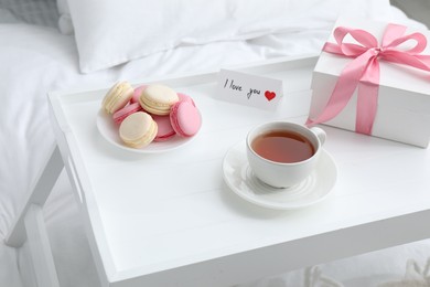 Photo of Tasty breakfast served in bed. Delicious eclairs, tea, gift box and I Love You card on tray