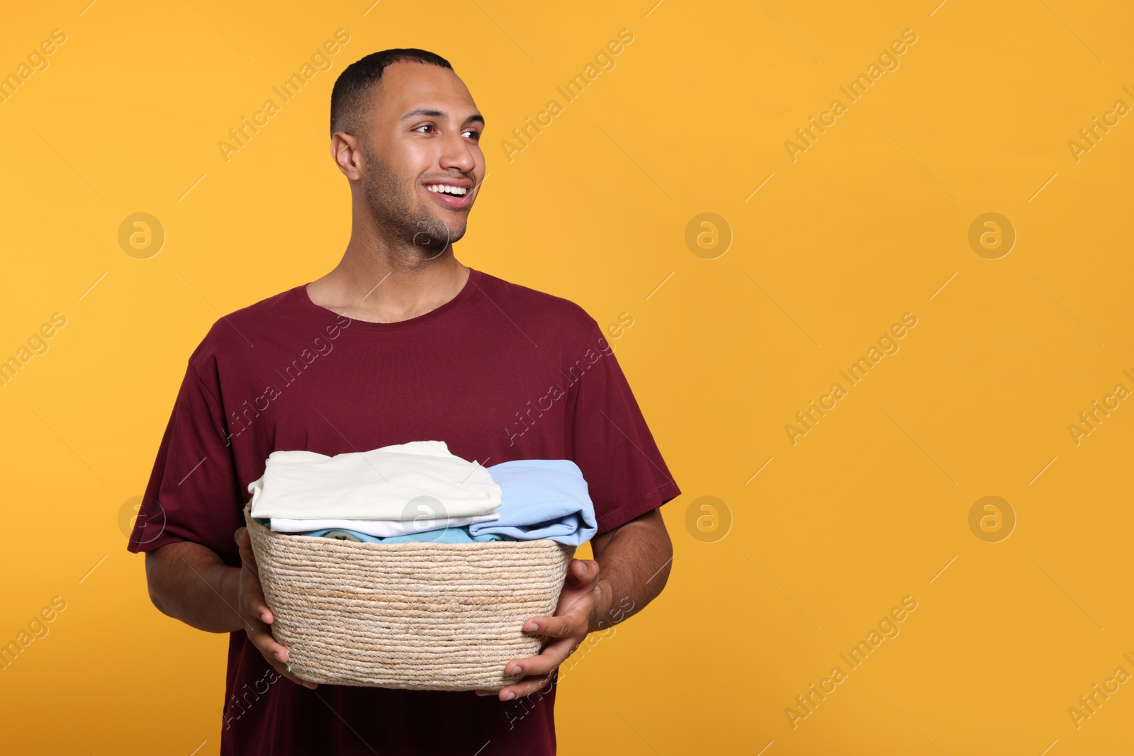 Photo of Happy man with basket full of laundry on orange background. Space for text