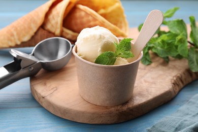 Photo of Delicious vanilla ice cream with mint in paper cup on light blue wooden table, closeup