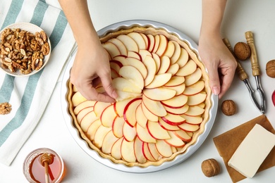 Photo of Woman putting apple slice into baking dish with dough to make traditional English pie at white table, top view