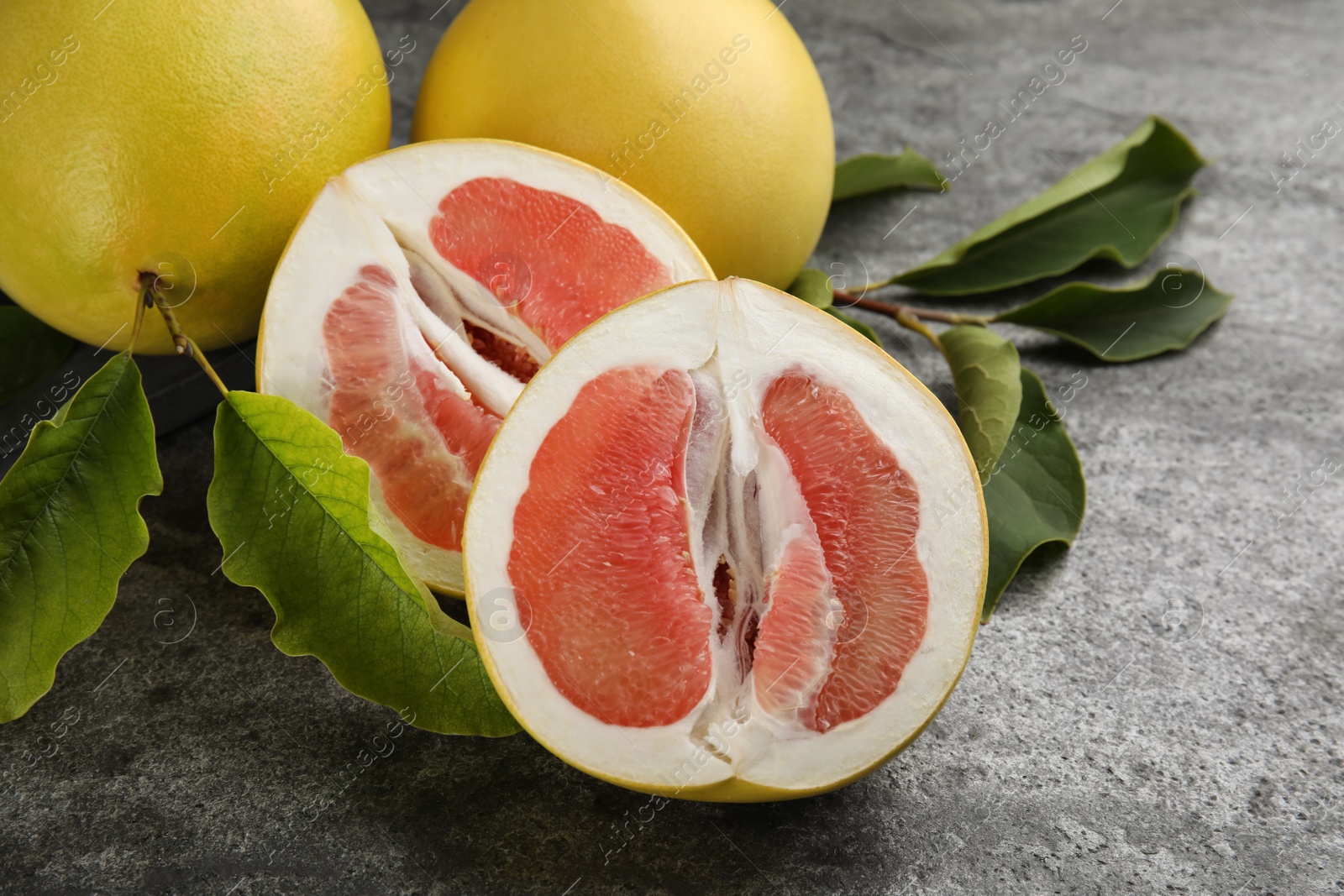 Photo of Fresh cut and whole pomelo fruits with leaves on grey table