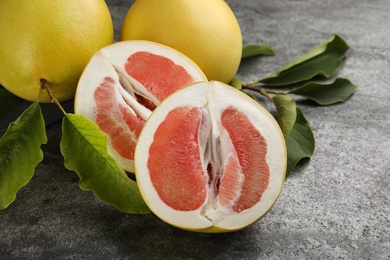 Photo of Fresh cut and whole pomelo fruits with leaves on grey table