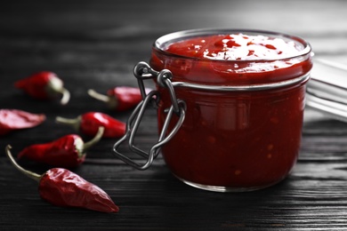 Photo of Jar of chili sauce on wooden table, closeup. Space for text