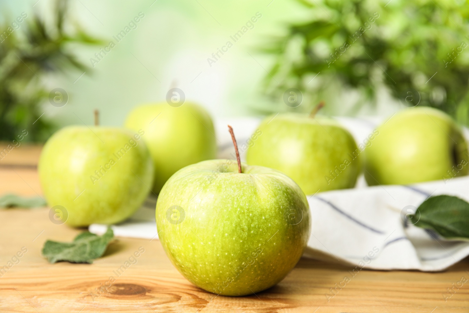 Photo of Fresh ripe green apples on wooden table against blurred background, space for text