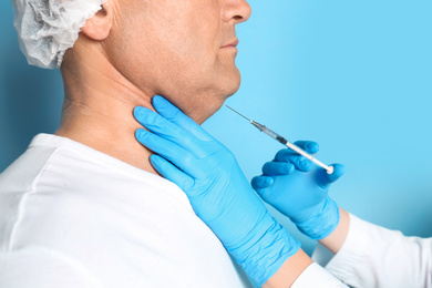 Mature man with double chin receiving injection on blue background, closeup