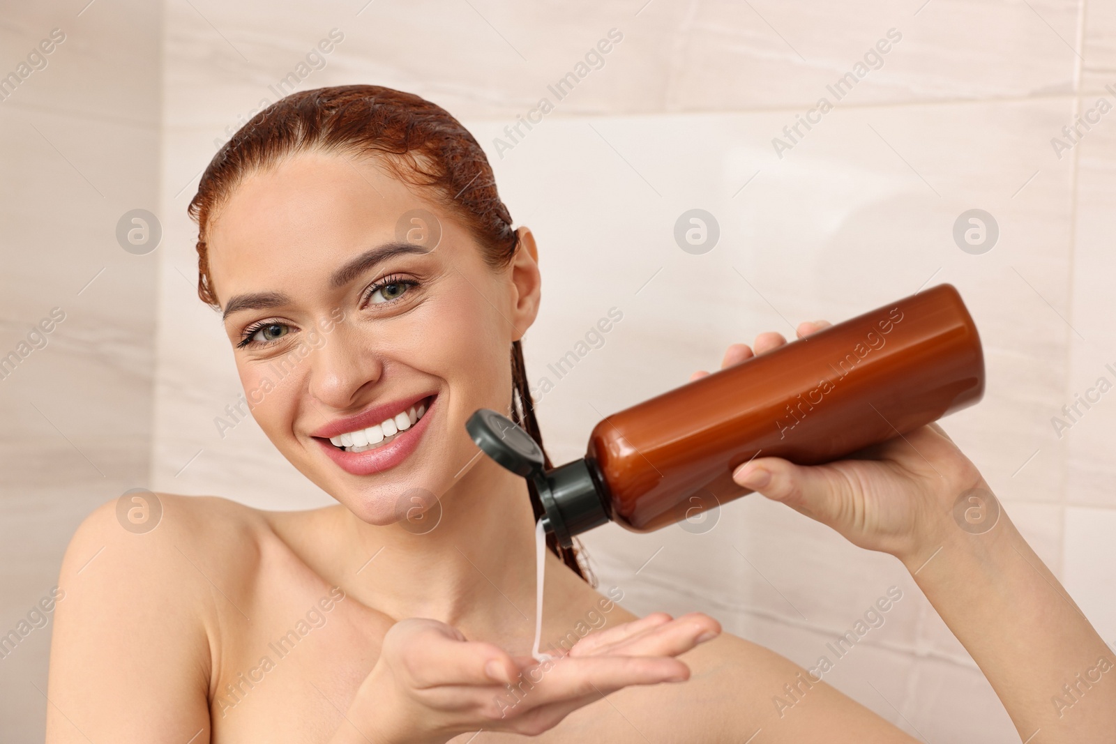 Photo of Happy young woman with bottle of shampoo washing her hair in shower