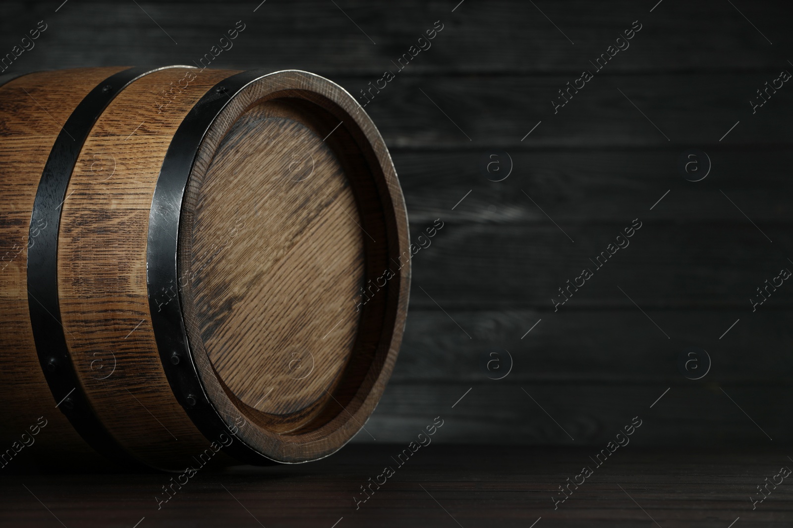 Photo of One wooden barrel on table near dark wall, closeup. Space for text