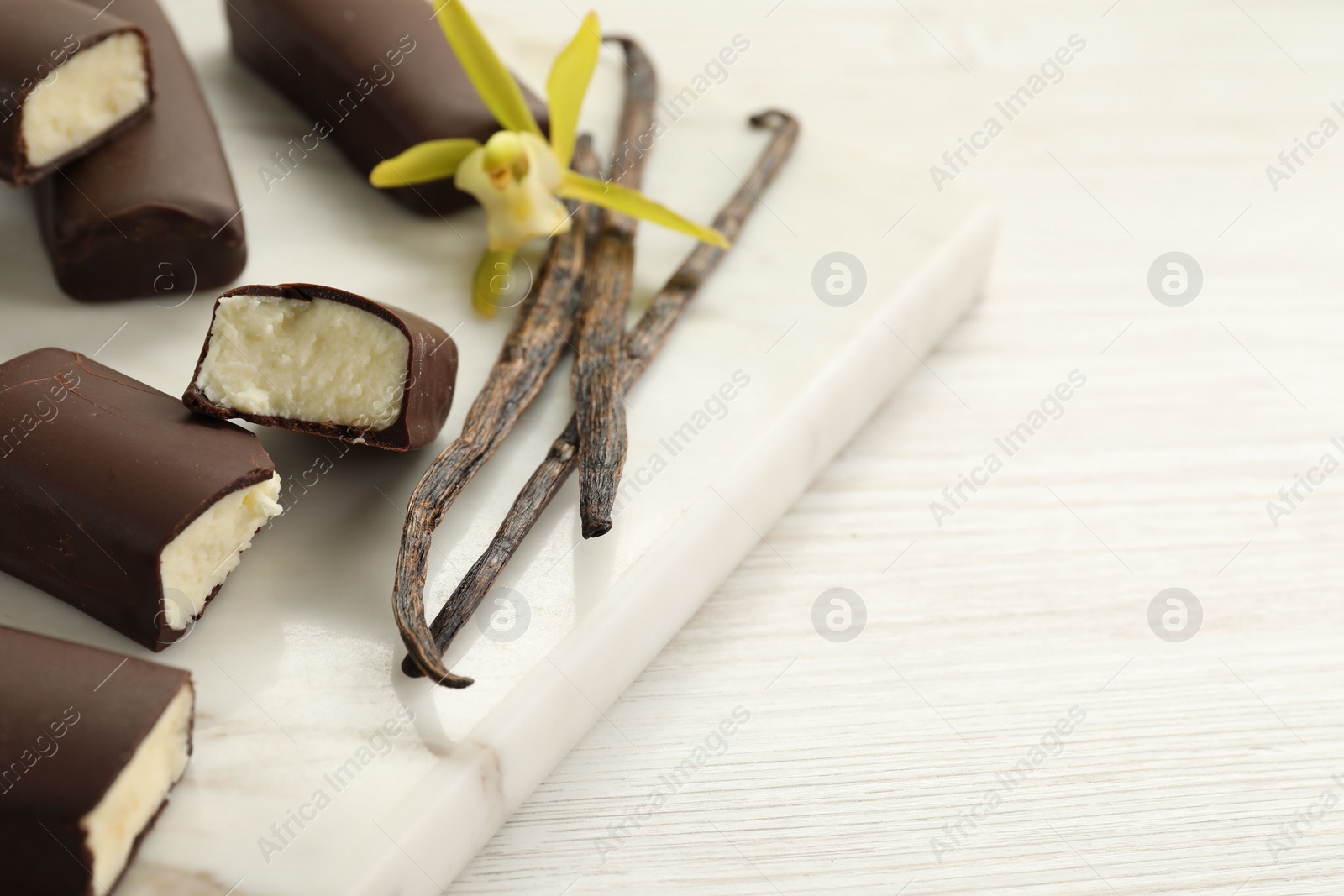 Photo of Glazed curd cheese bars, vanilla pods and flower on white wooden table, closeup. Space for text