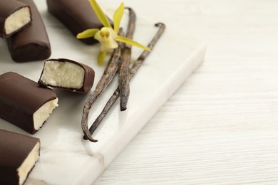 Photo of Glazed curd cheese bars, vanilla pods and flower on white wooden table, closeup. Space for text