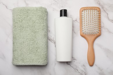 Shampoo bottle, towel and hair brush on white marble table, flat lay