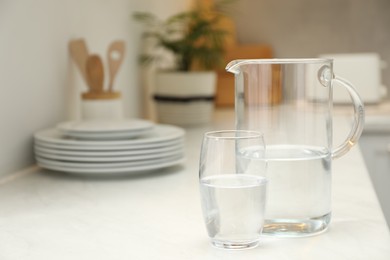 Photo of Jug and glass with clear water on white table in kitchen, space for text