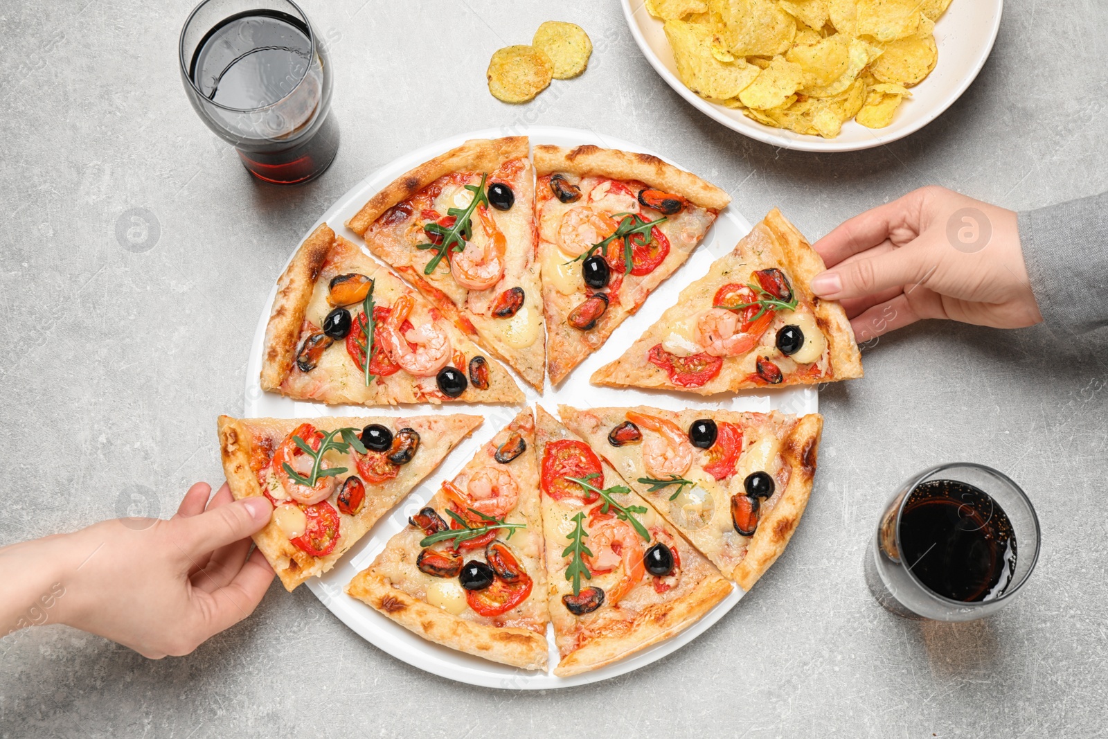 Photo of People taking slices of tasty pizza with seafood at light grey table, top view