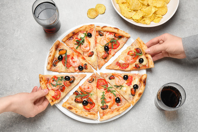 People taking slices of tasty pizza with seafood at light grey table, top view