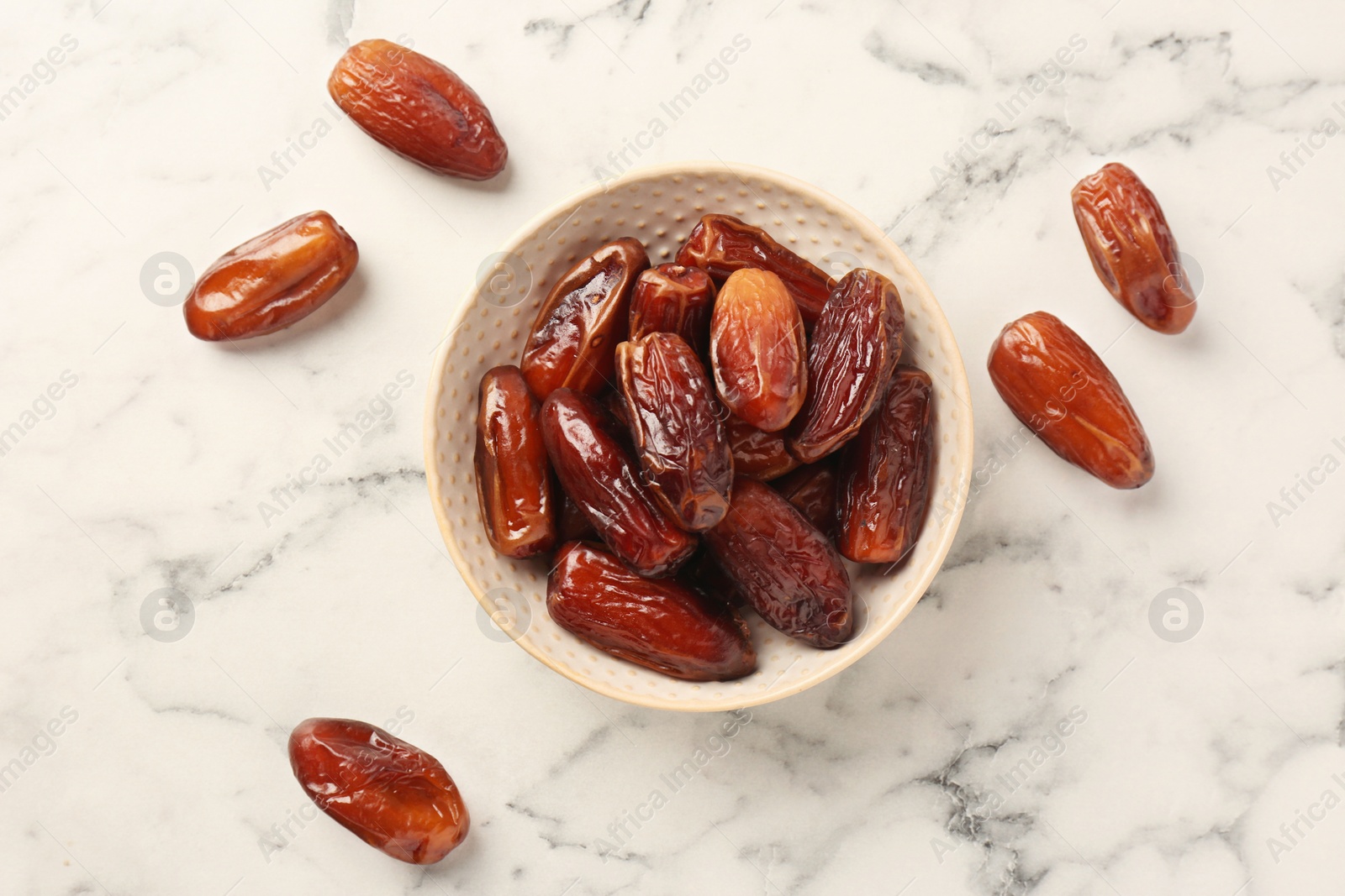 Photo of Sweet dried dates in bowl on white marble table, flat lay