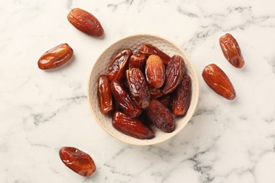 Sweet dried dates in bowl on white marble table, flat lay