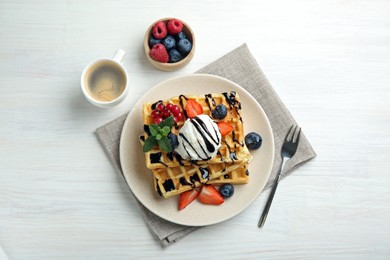Delicious Belgian waffles with ice cream, berries and chocolate sauce served on white wooden table, flat lay