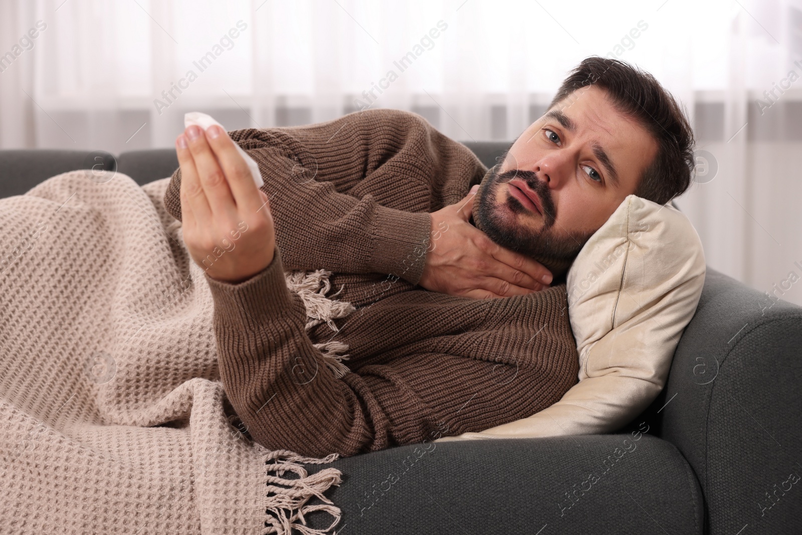 Photo of Sick man with tissue lying on sofa at home. Cold symptoms