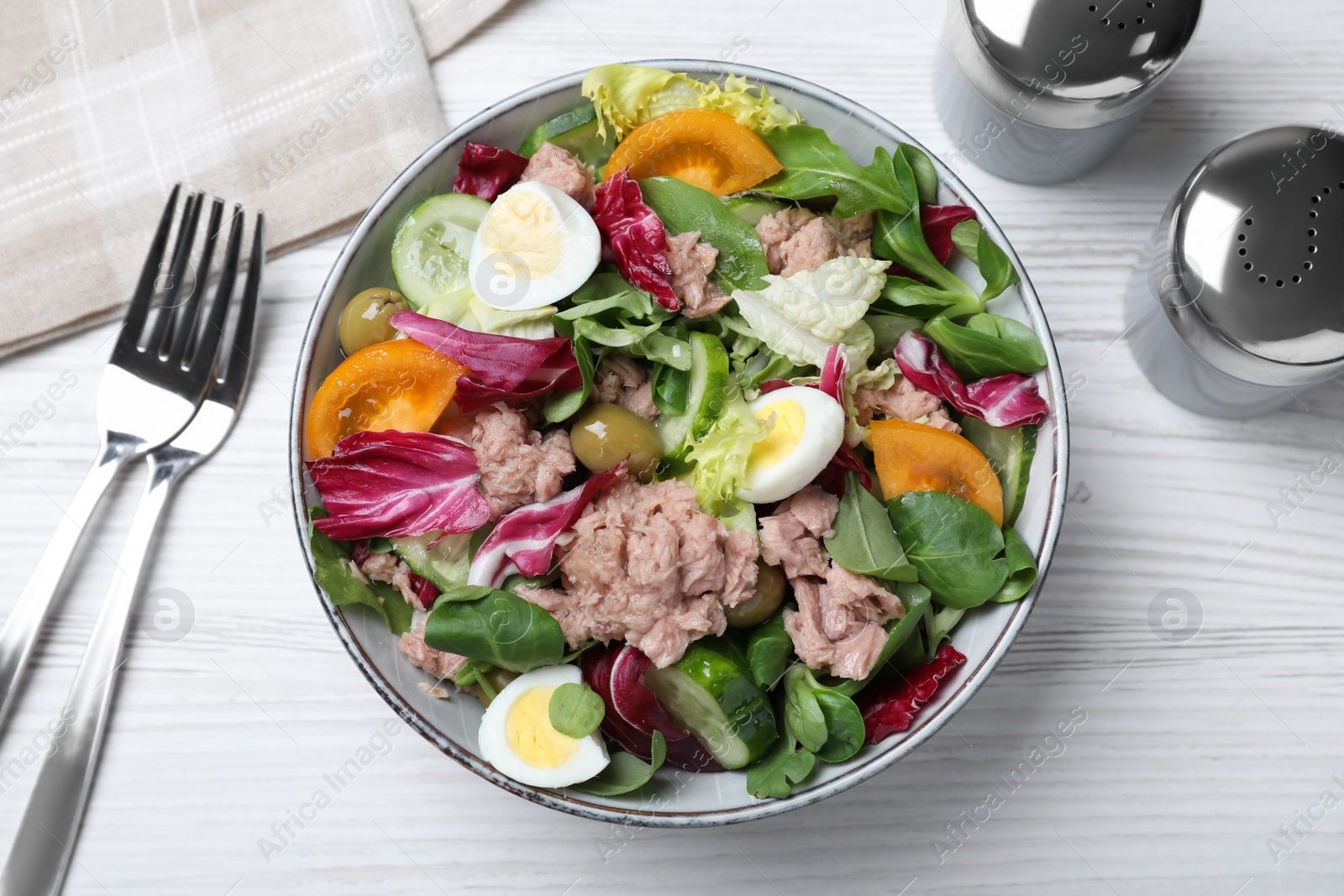 Photo of Bowl of delicious salad with canned tuna and vegetables served on white wooden table, flat lay