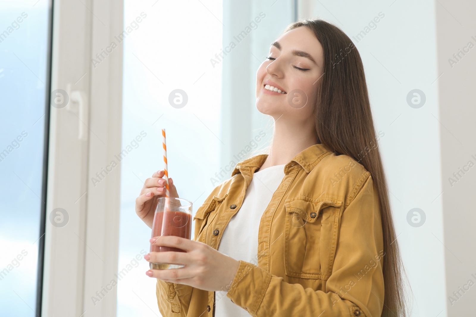 Photo of Beautiful young woman with delicious smoothie near window indoors. Space for text