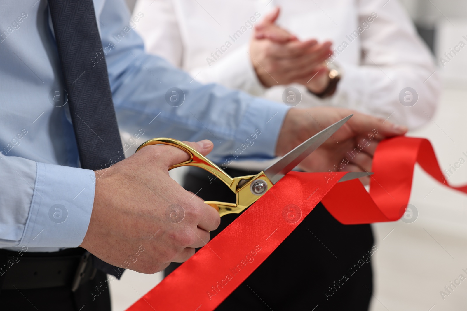 Photo of Man cutting red ribbon with scissors on blurred background, closeup