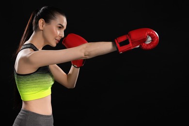 Photo of Beautiful woman in boxing gloves training on black background