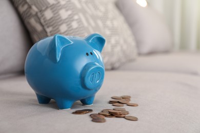 Blue piggy bank and coins on grey sofa