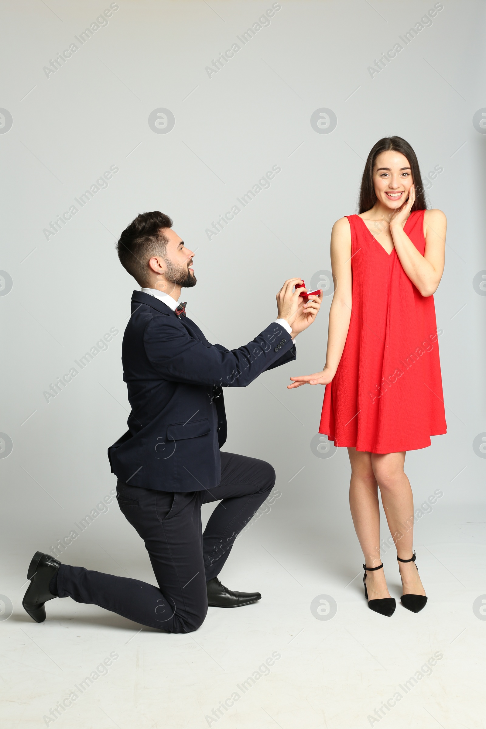 Photo of Man with engagement ring making marriage proposal to girlfriend on light grey background