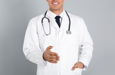 Happy male doctor offering handshake on light grey background, closeup