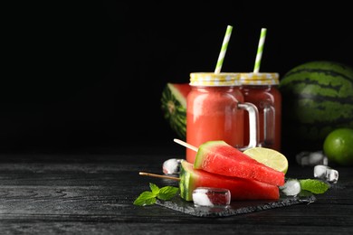 Photo of Slate board with juicy watermelon, ice and lime on black wooden table, space for text