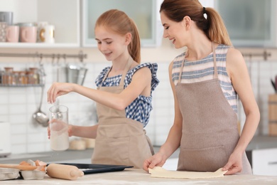 Photo of Mother and her daughter making dough at table in kitchen