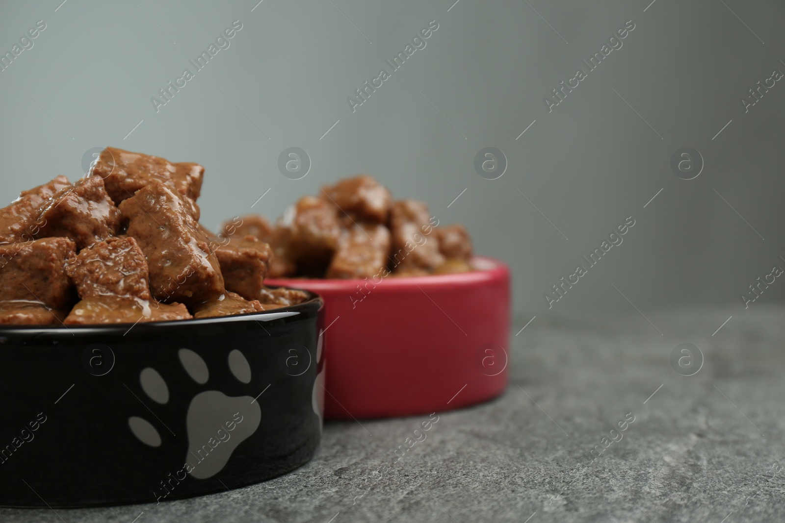 Photo of Wet pet food in feeding bowls on grey table, closeup. Space for text